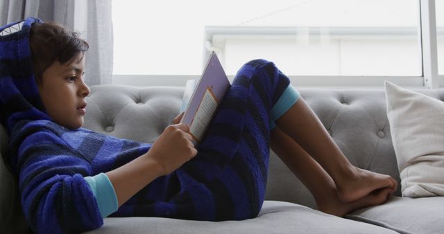 Child in Blue Striped Hoodie Relaxing on Couch Reading a Book - Download Free Stock Images Pikwizard.com