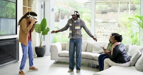 Diverse friends playing with virtual reality headsets in modern living room lounge
