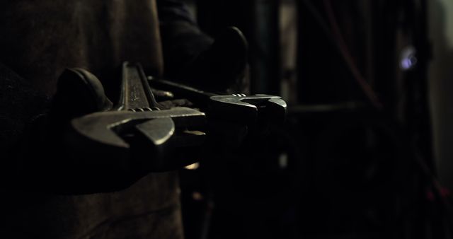 Close-up view of mechanic's hands holding large wrenches in dim-lit workspace, suitable for themes on repair, maintenance, mechanical work, industrial settings, and manual labor. Ideal for illustrating skill and craftsmanship in mechanical professions, tool use, and industrial work environments.