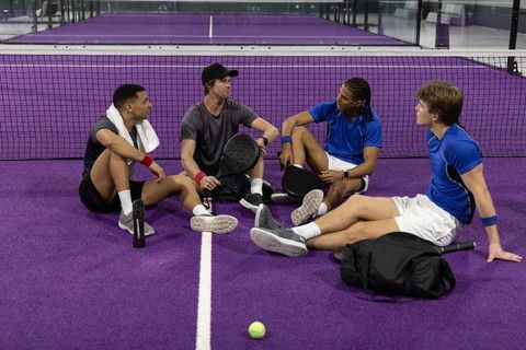 Padel team break on purple court resting and chatting, four diverse male players
