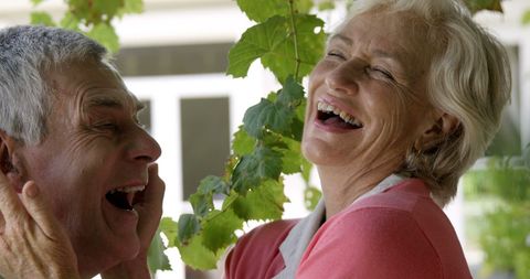 Joyful senior couple laughing under green leaves