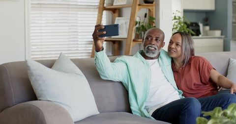 African American couple taking selfie on modern cozy living room sofa