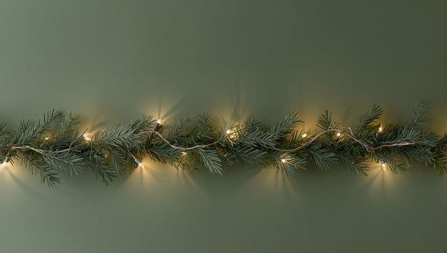 Minimalist pine garland with warm LED fairy lights on muted green wall for holiday decor