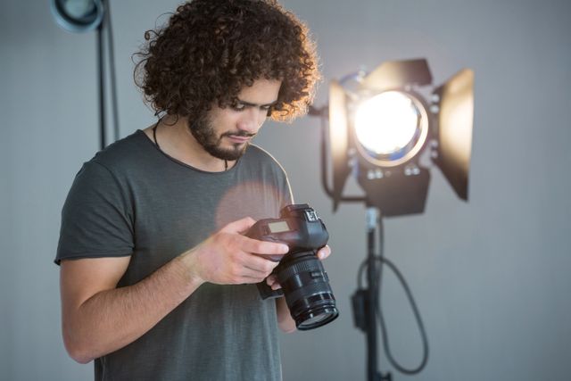 Photographer with curly hair reviewing shots on camera in a professional studio with lighting equipment. Ideal for use in articles about photography, creative professions, studio setups, or behind-the-scenes looks at photo shoots.