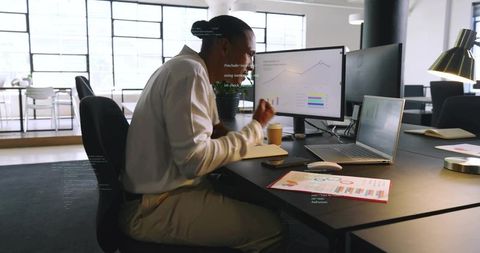 Professional reviewing analytics on dual monitors in bright open-plan office workspace