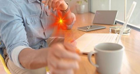 Man Reaching Toward Desk Foreground in Home Workspace with Laptop, Mug and Lens Flare