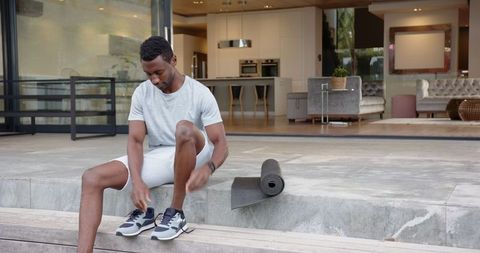 Man preparing for exercise outdoors at modern home with yoga mat and watch