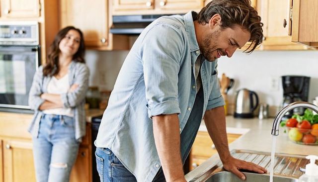 Stressed man leaning on kitchen sink while partner watching, domestic tension and emotion