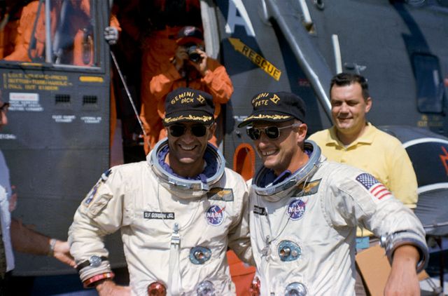 Two astronauts, Charles Conrad Jr. and Richard F. Gordon Jr., smiling excitedly after the Gemini 11 mission, standing in front of the recovery helicopter that brought them to the USS Guam. The joy and triumph on their faces emphasize the success of their mission. This image is perfect for use in articles, presentations, or documentaries about space exploration, NASA history, team dynamics, and scientific achievements in space missions.