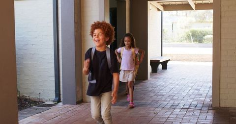 Playful students walking through sunlit school corridor with backpacks on brick walkway