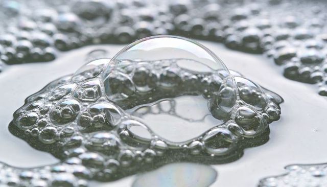 Macro soap bubble cluster shimmering on water surface with iridescent dome and soft bokeh