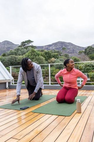 African american friends practicing partner stretches on rooftop deck with mountain view