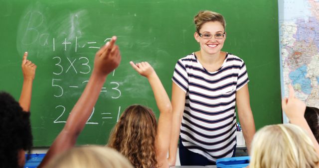 Happy caucasian female teacher and diverse elementary school pupils with hands raised in maths class. Education, childhood, teaching, learning, school and work, unaltered.