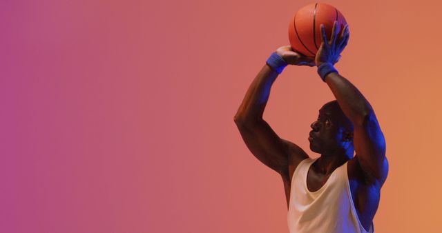 Image of african american male basketball player throwing ball on pink to orange background. Sports and competition concept.