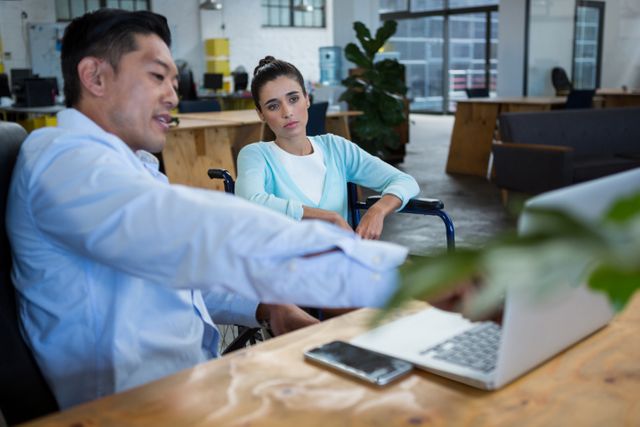 Businessman and disabled woman discussing over laptop in office