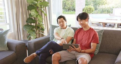 Asian Father and Teenage Son Bonding in Living Room with Tablet