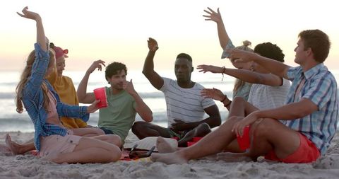 Diverse friends playing game on beach at sunset in slow motion