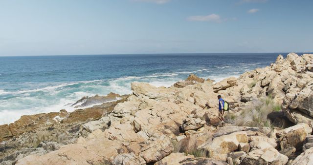 Hiker exploring rocky coastline with vast ocean in the background on a clear day; perfect for promoting outdoor adventure activities, travel destinations, and nature excursions.