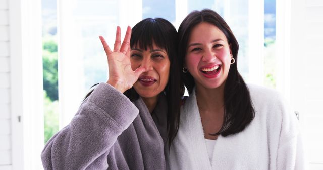 Portrait of happy biracial mother and adult daughter in bathrobes having fun, laughing, slow motion - Download Free Stock Photos Pikwizard.com