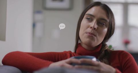 Young woman holding mug gazing pensively while leaning on sofa in cozy living room