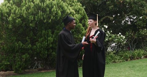Graduates celebrating outdoors in caps and gowns holding diplomas in garden