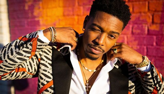 Sunlit urban fashion portrait of man pulling collar wearing patterned blazer and jewelry