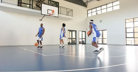 Basketball teammates practicing dribbling on indoor court