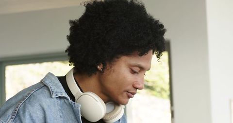 African american man wearing white headphones and denim jacket contemplating window