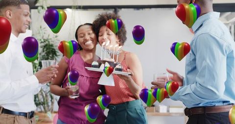 Office birthday celebration with woman blowing out cupcakes and rainbow heart graphics