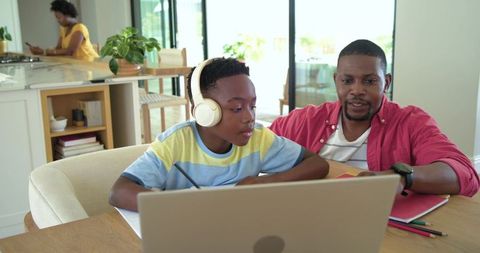 African american father helping son with remote learning on laptop at home