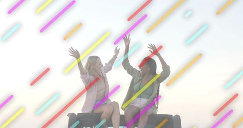 Two friends celebrating on car trunk at sunset with colorful overlay