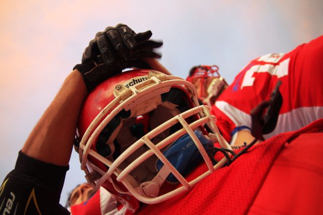 Football player in red gear adjusting helmet while preparing for game. Ideal for sports illustrations, team dynamics, competitive spirit, athletic performance imagery