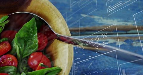 Spoon reflecting data hud over rustic tomato basil salad in wooden bowl on blue table