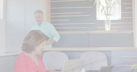 Senior couple working from home kitchen woman typing on laptop while partner watches