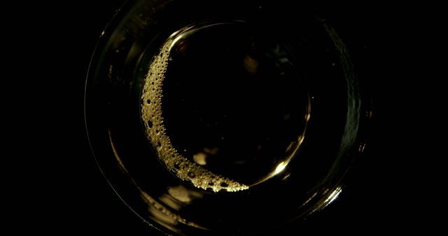 This image captures a top view of a glass of beer, showcasing the frothy bubbles on the surface. The dark background highlights the golden liquid and its effervescence. This photo is perfect for use in advertisements or marketing for bars, breweries, or any event where beverages are featured. It can also be used in designs and articles focusing on beer, drinking culture, and social gatherings.