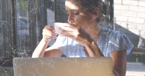 Young Woman Drinking Coffee and Working on Laptop in Sunlit Space
