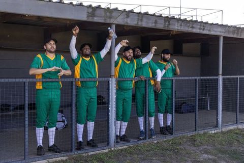 Dugout team cheering celebrating leaning on fence green baseball uniforms diverse players