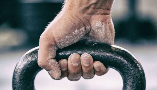 Chalk-coated hand gripping rusted kettlebell handle close-up conveying strength workout