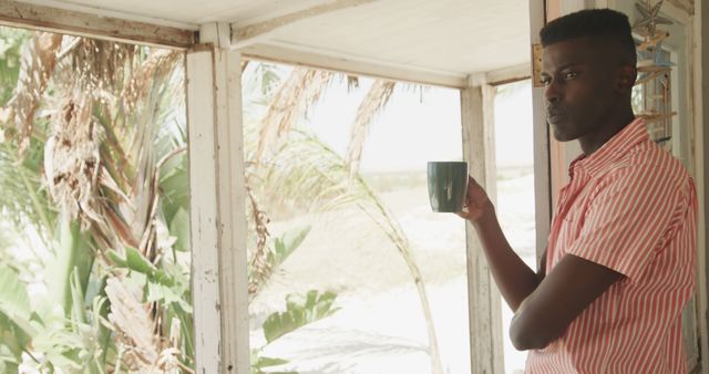 African-American man enjoying morning coffee on tropical veranda. Ideal for wellness, lifestyle, relaxation, summer themes, and advertising peaceful or vacation moments.