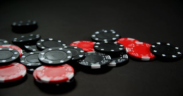 Red and black poker chips scattered on a black surface. Ideal for use in articles about gambling, casino games, betting strategies or gaming concepts. Suitable for advertisements, blog posts, and promotional materials related to casinos and online gaming platforms.