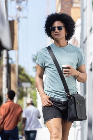Urban casual african american man walking with coffee and messenger bag in sunny city
