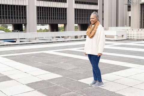 Senior woman standing on rooftop plaza wearing cable knit sweater and scarf, urban copy space