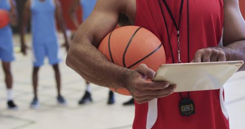 Male basketball coach reviewing plays with players nearby