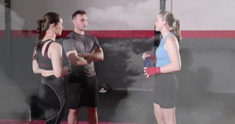 Female coach leading boxing training trio in industrial gym with hand wraps and water bottle