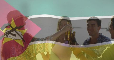 Friends celebrating and toasting with beer on sunny beach with mozambique flag overlay