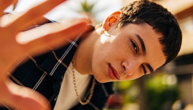 Leaning youth reaching toward camera in sunlit portrait wearing shirt and septum ring