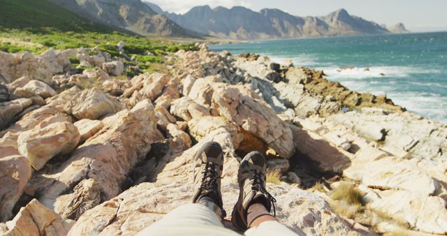 Low section of biracial man with prosthetic leg trekking, sitting on rocks taking a rest by the sea. Long distance walking, fitness, challenge, disability, nature and healthy outdoor lifestyle.