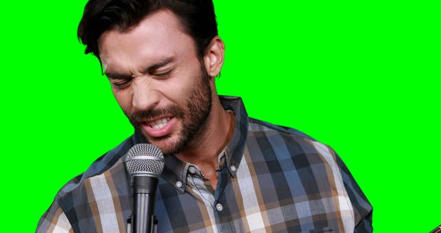 Man singing passionately into a microphone while standing against a green screen background, suitable for musical performances, karaoke events, sound recording studios, and promotional videos in entertainment industry. Versatile for editing and placing over different backgrounds.