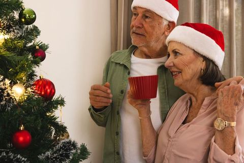 Senior Couple Wearing Santa Hats Celebrating Christmas by Tree