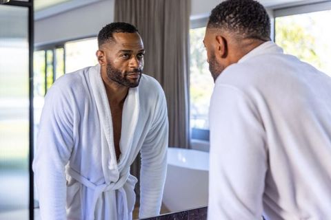 Middle-aged african american man reflecting in bathroom mirror wearing white bathrobe